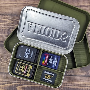 May include: A green metal storage case with a silver lid that says "VTOIDE" on it. The case has four compartments that hold various memory cards, including a micro SD adapter, a 4GB SD card, a 32GB SD card, and an xD-Picture Card.