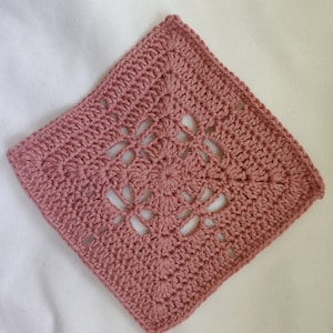 May include: A square crocheted doily in a dusty rose color with a lacy pattern.