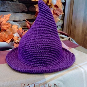 May include: A handmade, purple crochet witch hat with a wide brim and a pointed top. The hat is made of a textured yarn and sits on a plaid surface. The word "PATTERN" is printed in red at the bottom of the image.