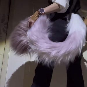 Peut inclure: Un accessoire circulaire et duveteux dans les tons lavande et blanc. L'article en fausse fourrure est maintenu, mettant en valeur sa texture et son dégradé de couleurs. L'accessoire semble être une queue ou une pièce décorative.