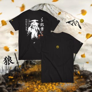 May include: Black t-shirts with Japanese-inspired graphics. One shirt features a white illustration and Japanese text on the front and back. The other shirt has a small yellow emblem on the front. The background includes a mountain and falling leaves.