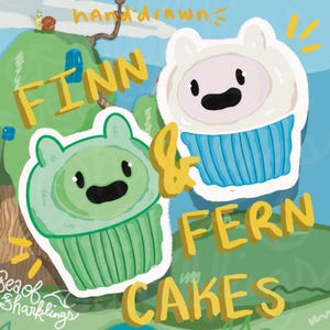 May include: Illustration of two cartoon cupcakes, one green and one white, with faces and the words "Finn & Fern Cakes." The green cupcake has a green frosting hat, and the white cupcake has a white frosting hat with a blue cupcake liner.