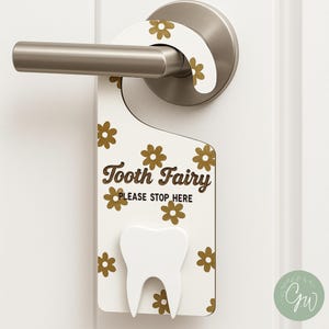 May include: A white door hanger with a gold floral pattern and the text "Tooth Fairy PLEASE STOP HERE." A white tooth shape is at the bottom. The door hanger is hanging on a silver door handle.