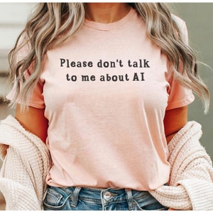 Puede incluir: Una camiseta rosa con el texto "Please don't talk to me about AI" impreso en negro.
