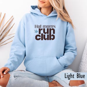 May include: Light blue hoodie with a front pocket and a drawstring hood. The text "Hot moms run club" is printed on the front in brown. The words "Light Blue" are printed at the bottom of the image.