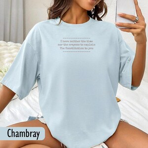 May include: Light blue chambray t-shirt with the text "I have neither the time nor the crayons to explain The Constitution to you." The shirt has short sleeves and a relaxed fit.