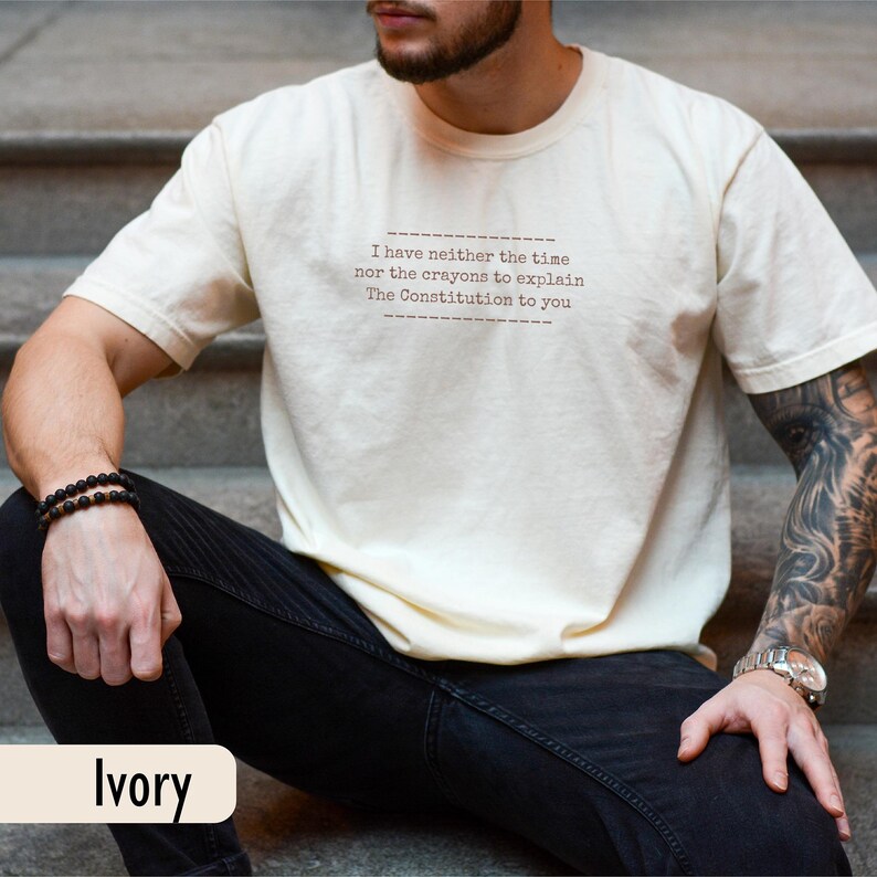 May include: Ivory-colored t-shirt with the text "I have neither the time nor the crayons to explain The Constitution to you." The shirt is a neutral color and has a relaxed fit. The word "Ivory" is printed at the bottom.