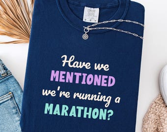 May include: A navy blue sweatshirt with the text "Have we MENTIONED we're running a MARATHON?" in white, purple, and teal. A silver necklace with a pendant is on the shirt. The sweatshirt is labeled "True Navy".