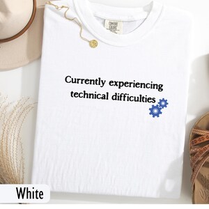 以下が含まれることがあります： 「Currently experiencing technical difficulties」というテキストと青い歯車のアイコンが書かれた白いTシャツです。