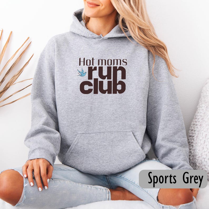 May include: A light gray hoodie with the text "Hot moms run club" in brown. A blue bird graphic is above the word "run". The hoodie has a front pocket and a drawstring hood. The bottom right corner of the image has the text "Sports Grey".