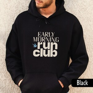 May include: Black hoodie with the text "EARLY MORNING RUN CLUB" in white, with a blue bird graphic. The hoodie has a drawstring hood and a front pocket. The word "Black" is printed at the bottom right.
