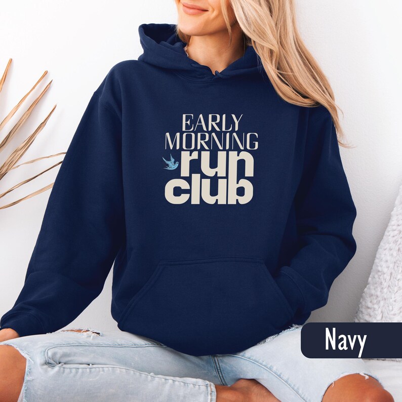 May include: Navy blue hooded sweatshirt with the text "EARLY MORNING run club" in white. The design includes a small blue bird graphic. The sweatshirt has a front pocket and a drawstring hood.