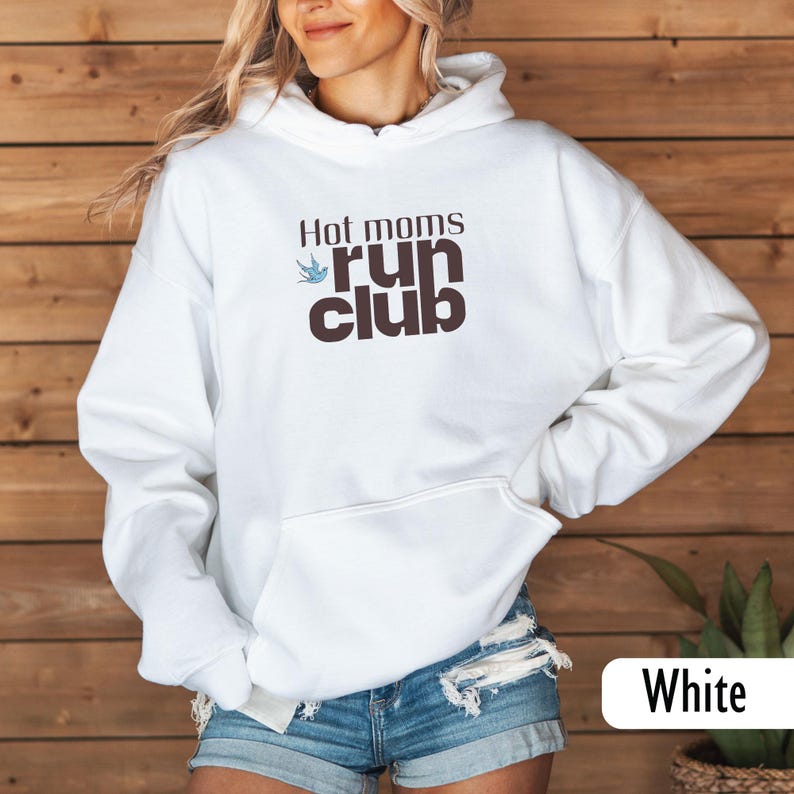 May include: White hooded sweatshirt with the text "Hot moms run club" in brown and blue. The sweatshirt has a front pocket and a drawstring hood. The text is in a casual font, and the design includes a small bird graphic.