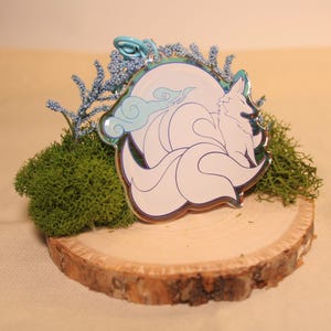 May include: A white nine-tailed fox with blue clouds, iridescent, on a wooden base with moss and blue flowers.