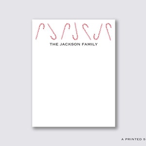 Könnte beinhalten: Weißer Notizblock mit roten und weißen Zuckerstangen-Illustrationen oben und dem Text "THE JACKSON FAMILY" in schwarzer Schrift.