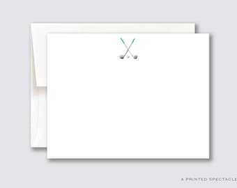 May include: A white card with a green and silver golf club design. The clubs are crossed and there are two golf balls.