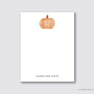 May include: A white card with a gingham pumpkin illustration and the text "CAROLINE KATE" printed in black.
