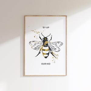 Puede incluir: Impresi&oacute;n art&iacute;stica enmarcada con una ilustraci&oacute;n estilizada de abeja en negro y dorado. La abeja tiene las alas extendidas y el texto "'EY UP OUR KID" est&aacute; debajo. Hay salpicaduras de pintura dorada.