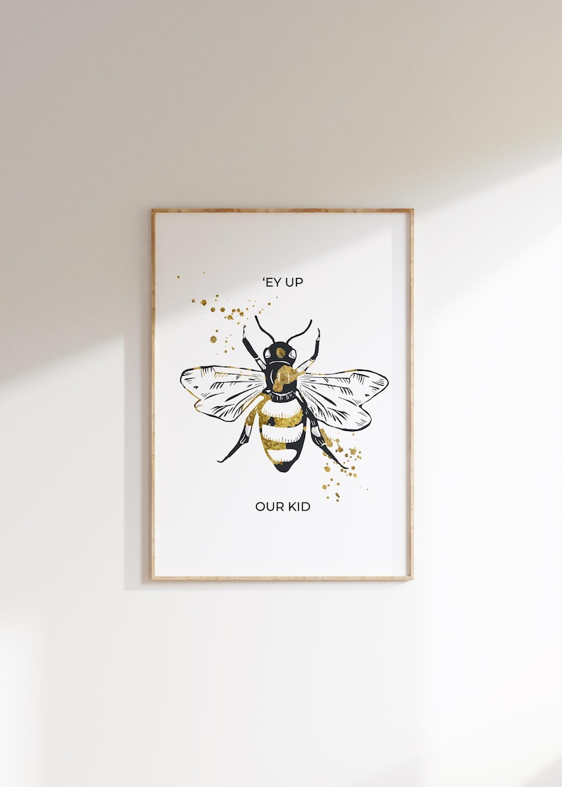 Puede incluir: Impresi&oacute;n art&iacute;stica enmarcada con una ilustraci&oacute;n estilizada de abeja en negro y dorado. La abeja tiene las alas extendidas y el texto "'EY UP OUR KID" est&aacute; debajo. Hay salpicaduras de pintura dorada.