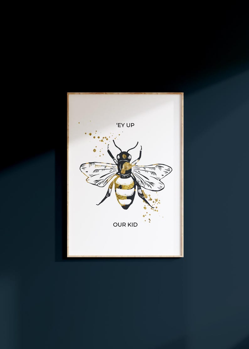 Puede incluir: Impresi&oacute;n art&iacute;stica enmarcada con una ilustraci&oacute;n de abeja en negro y dorado. El texto dice "'EY UP OUR KID". Salpicaduras de pintura dorada acent&uacute;an el dise&ntilde;o. El marco es de color madera clara.