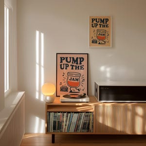 May include: A room interior features two framed posters with the text "PUMP UP THE JAM" and a cartoon jar of jam. A record player sits on a wooden cabinet with a collection of vinyl records. A white and orange globe lamp is on the cabinet.