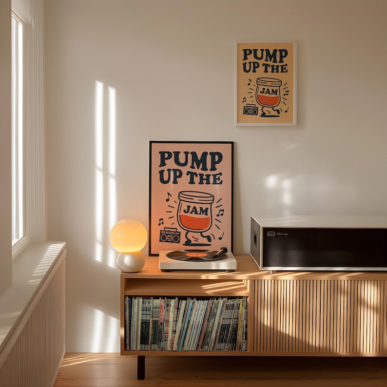 May include: A room interior features two framed posters with the text "PUMP UP THE JAM" and a cartoon jar of jam. A record player sits on a wooden cabinet with a collection of vinyl records. A white and orange globe lamp is on the cabinet.