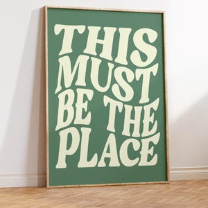 Puede incluir: Una impresión enmarcada con fondo verde y texto blanco que dice "This Must Be The Place".