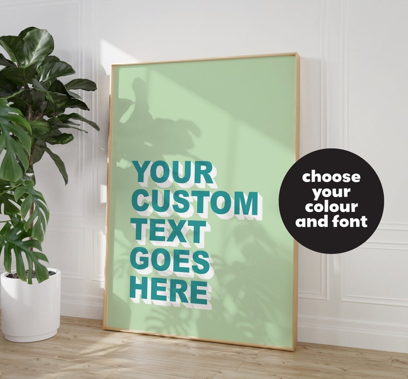 May include: A framed poster with a light green background and white shadowing. The text "YOUR CUSTOM TEXT GOES HERE" is in a teal blue color with a white outline. The text is in a bold, sans-serif font. A black circle with white text says "choose your colour and font".