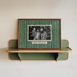Puede incluir: Una fotografía en blanco y negro enmarcada de una familia, con el texto "Making memories with Dad", se muestra en una estantería verde y de madera. El marco tiene un fondo a rayas verdes y blancas.