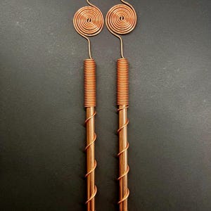 Può includere: Due orecchini in filo di rame con un design a spirale. Gli orecchini sono lunghi e hanno una bobina nella parte superiore.
