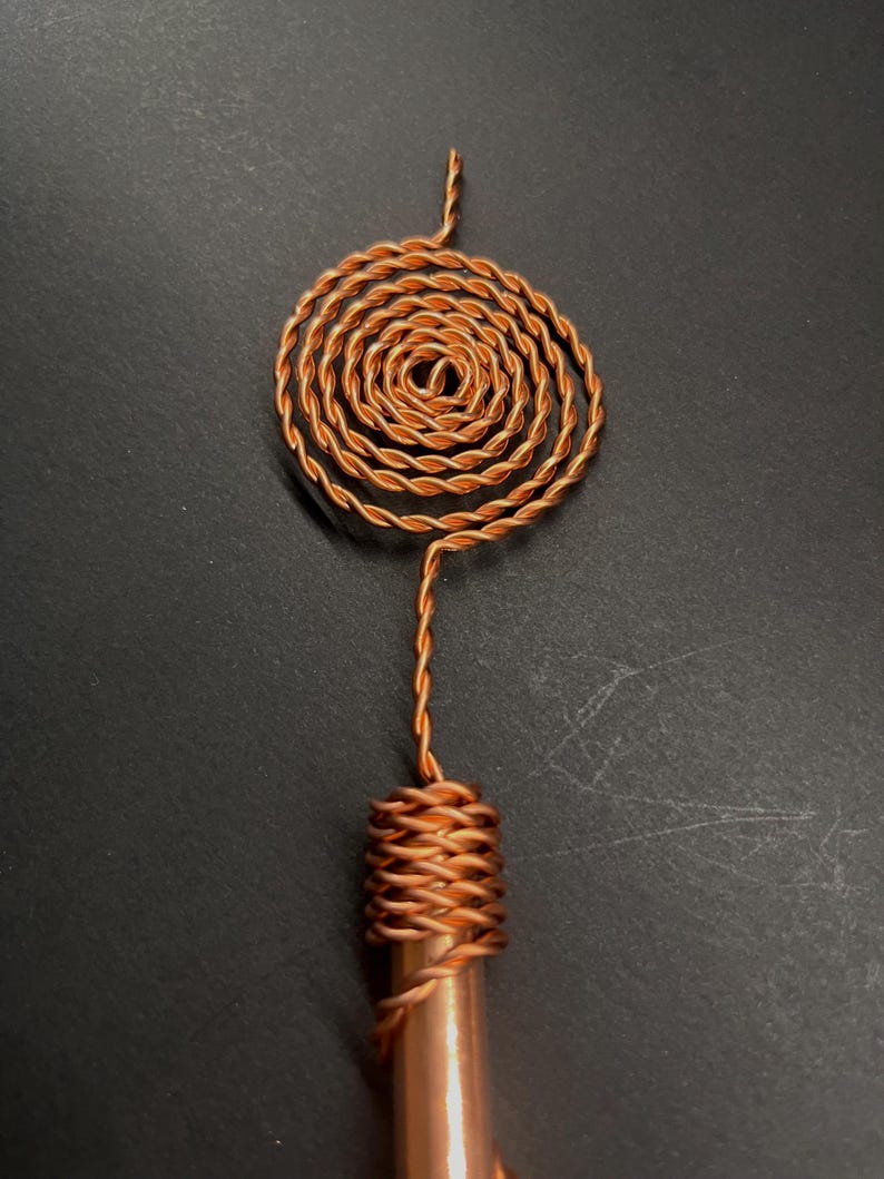 May include: A copper-colored, handmade pendant with a spiral design. The pendant features a coiled spiral at the top, connected to a wrapped cylindrical base. The metal has a warm, reddish-brown hue.