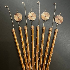 May include: Eight gold-colored metal stirring sticks with a spiral design at the top. The sticks are arranged in a fan shape.
