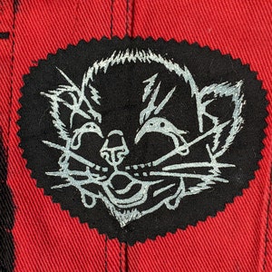 May include: A black and white embroidered patch of a cat's face with a white outline. The patch is sewn onto a red fabric background.