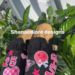 May include: Black suede clogs with pink and white patches. The patches include a skull and crossbones, a butterfly, hearts, stars, and the word "Senior". One clog has the number "25" on it.