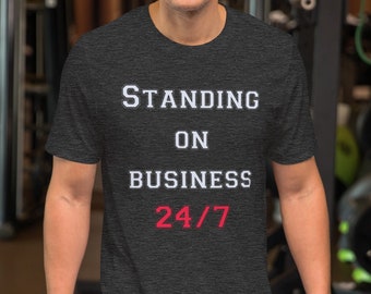 May include: A dark gray t-shirt with the text "STANDING ON BUSINESS 24/7" in white lettering. The number "24" is in red.