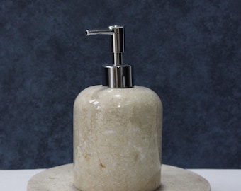 May include: A beige marble soap dispenser with a chrome pump sits on a beige marble base.