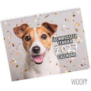 Può includere: Un calendario da parete a spirale con il ritratto di un Jack Russell Terrier dal pelo marrone e bianco, con la bocca aperta e la lingua rosa. Lo sfondo è grigio chiaro con coriandoli dorati sparsi. Il testo recita: JACK RUSSELL TERRIER 2027 CALENDAR.