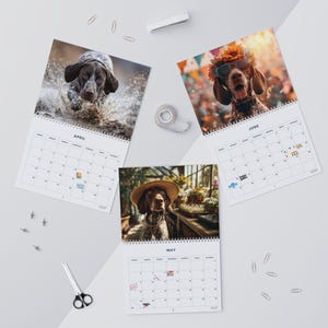 May include: Three wall calendar pages for April, May, and June featuring German Shorthaired Pointer dogs. The April page shows a dog splashing in water, May shows a dog wearing a straw hat, and June shows a dog wearing sunglasses and a flower crown.