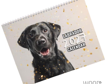 Può includere: Un calendario da parete 2027 con un Labrador nero sulla copertina. Il cane è ritratto dal petto in su con la bocca aperta su uno sfondo chiaro con accenti di coriandoli dorati. Il testo riporta LABRADOR 2027 CALENDAR e WOOF.