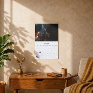 May include: A wall calendar featuring a dark, atmospheric image of a figure in a hat near a candlelit pot for the month of October. The calendar has a white grid with black text, a spiral binding at the top, and small icons on specific dates.