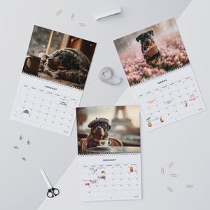 K&ouml;nnte beinhalten: Drei Wandkalender mit Rottweiler-Fotografien f&uuml;r Januar, Februar und M&auml;rz. Jede Seite zeigt ein Monatsraster mit kleinen bunten Symbolen f&uuml;r Feiertage. Die Kalender sind spiralgebunden und mit B&uuml;robedarf arrangiert.