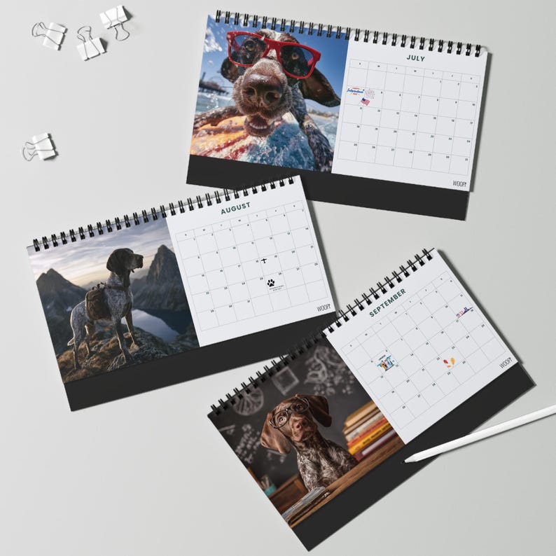May include: Three spiral-bound desk calendars featuring dog photography. The July page shows a dog in red glasses, August shows a dog on a mountain, and September shows a dog with glasses near books. Each calendar has a black base and white pages.