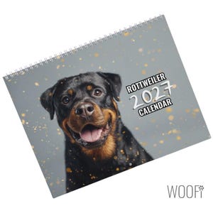 Könnte beinhalten: Ein spiralgebundener Rottweiler-Kalender für 2027 mit dem Porträt eines schwarz-braunen Rottweilers mit offenem Maul auf grauem Hintergrund mit goldenen Sprenkeln. Der Text auf dem Cover lautet ROTTWEILER 2027 CALENDAR in weißer und schwarzer Schrift.