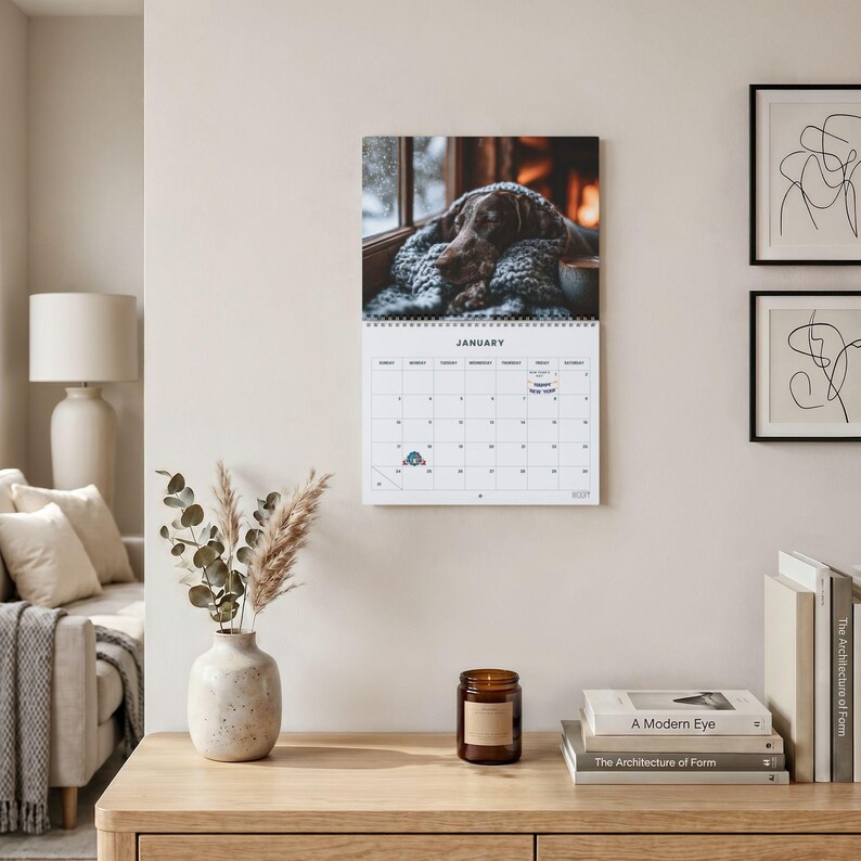 May include: A wall calendar for January featuring a photograph of a brown dog resting on a gray knitted blanket. The calendar grid includes the month title, days of the week, numbered dates, and small icons marking New Year's Day and other events.