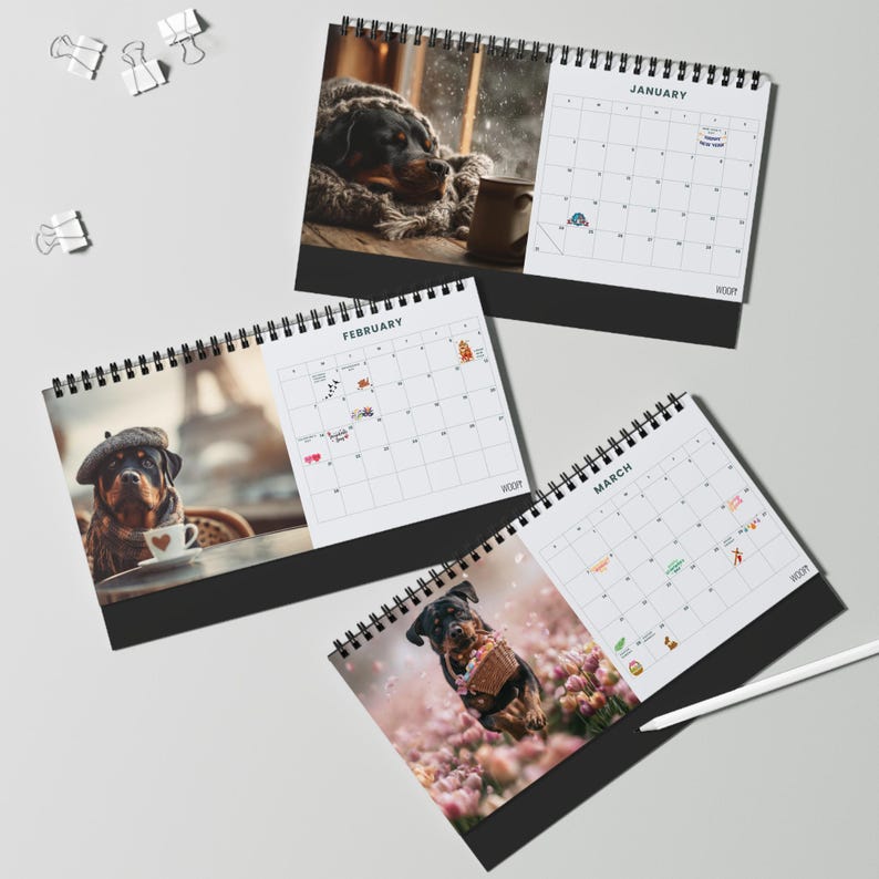 K&ouml;nnte beinhalten: Drei spiralgebundene Tischkalender mit Rottweiler-Fotografien f&uuml;r Januar, Februar und M&auml;rz. Jede Seite zeigt ein Monatsraster mit kleinen Symbolen und dem Monatsnamen oben. Ein wei&szlig;er Eingabestift liegt neben dem Kalender f&uuml;r M&auml;rz.
