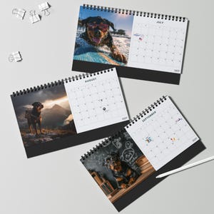 K&ouml;nnte beinhalten: Drei spiralgebundene Tischkalender mit Rottweiler-Fotografien f&uuml;r Juli, August und September. Jede Seite zeigt ein Monatsraster mit kleinen Symbolen und dem Text WOOF. Wei&szlig;e B&uuml;roklammern und ein wei&szlig;er Eingabestift liegen daneben.