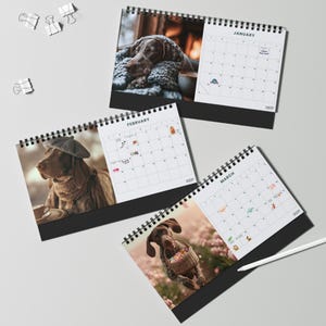 May include: Three spiral-bound desk calendars featuring dog photography for January, February, and March. Each page displays a monthly grid with dates and small icons. The January page shows a dog resting, February shows a dog in a beret, and March shows a dog with a basket. White binder clips are scattered nearby.