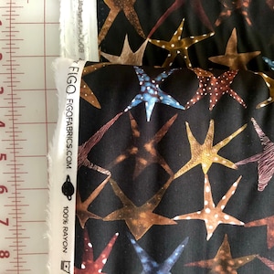 Könnte beinhalten: Schwarzer Stoff mit einem sich wiederholenden Muster aus braunen, blauen und goldenen Seesternen. Der Stoff hat ein weißes Etikett mit dem aufgedruckten Text "FIGO FIGFABRICS.COM 100% RAYON".