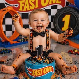 May include: A baby covered in cake sits in front of a birthday cake with the words "FAST ONE" and a Hot Wheels logo. The cake is blue with orange and black accents. The baby wears suspenders and a bow tie.