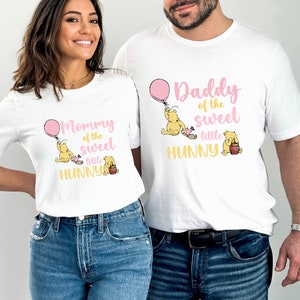 May include: Two white t-shirts with a pink balloon and Winnie the Pooh characters. The text on the shirts reads "Mommy of the sweet little Hunny" and "Daddy of the sweet little Hunny".